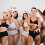 group of multiethnic women, afro, caucasian, brunette and redhead, of different ages, posing in underwear laughing and looking at camera, having fun together, studio shot.