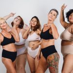 group of multiethnic women, afro, caucasian, brunette and redhead, of different ages, posing in underwear laughing and looking at camera, having fun together, studio shot.